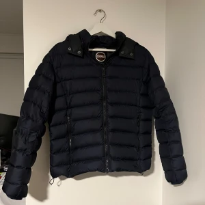 Svart dunjacka från Colmar - Säljer en snygg mörkblå dunjacka från Colmar i mycket bra skick. Jackan har en dragkedja framtill och är perfekt för kalla dagar. Den är långärmad och har en huva för extra värme. Perfekt för vintern och hösten!