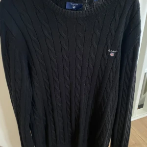 Stickad Gant tröja - Säljer en stilren svart stickad tröja från GANT i mycket bra skick. Tröjan har ett klassiskt flätmönster och rund halsringning. Perfekt för både höst och vinter, och funkar lika bra till vardags som till fest. 🖤 Hör av er vid frågor eller om du vill ha fler bilder. 👊