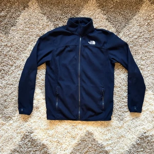 Marinblå fleecejacka, The North Face - Säljer en marinblå fleecejacka från The North Face i mycket bra skick. Jackan har en dragkedja framtill och två praktiska fickor med dragkedjor. Perfekt för kyliga höst- och vårdagar. Den är långärmad och har en normal passform. Superbekväm och stilren!