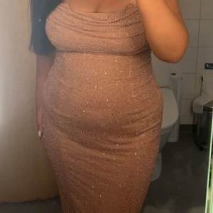 Glittrig beige klänning - Säljer en superfin glittrig beige klänning i tight passform. Den är axelbandslös och perfekt för festliga tillfällen. Klänningen har en elegant drapering över bysten och är gjord i ett bekvämt material som formar sig fint efter kroppen.