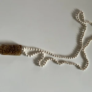 Vitt halsband med dekorativt hänge - Säljer ett unikt vitt halsband med ett rektangulärt hänge. Hänget har ett intrikat mönster i brunt och guld, vilket ger en elegant touch. Perfekt för att lyfta en enkel outfit eller som ett statement piece på festen. 