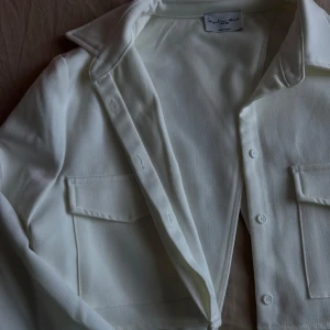 Vit skjorta med fickor - Snygg vit skjorta med klassisk krage och knappar framtill. Perfekt för både vardag och fest. Skjortan är i ett mjukt material och helt oanvänd. 