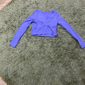 Lila ribbad omlottopp - Säljer en snygg lila ribbad omlottopp med långa ärmar. Perfekt för både vardag och fest! Toppen har en omlottdesign som ger en smickrande passform. Den är i mycket bra skick och redo för en ny ägare. Passar perfekt till jeans eller kjol!