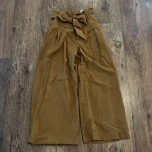 Bruna vida byxor med knytband - Säljer ett par snygga bruna/ senapsgula byxor med hög midja och knytband i midjan. De har en loose och wide passform som ger en avslappnad stil. Perfekta för både vardag och fest! 🧡obs! Har lagt upp dem 5 cm men har lossnat se bild. 