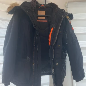 Svart vinterjacka Äkta Parajumper - Säljer en svart Parajumpers vinterjacka i mycket bra skick. Jackan har en avtagbar huva med pälsdetaljer och flera praktiska fickor. Den är långärmad och har en dragkedja framtill. Perfekt för kalla vinterdagar! ❄️Finns 2 av dessa jackor fast i två olika storlekar. En i S och den ena i M. En köpt för 4500kr