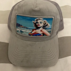 Grå keps revenite - Snygg grå keps från Revenite med ett coolt popkonstmotiv på framsidan. Kepsen har ett nätmaterial baktill för bra ventilation och en justerbar passform. Perfekt för sommarens alla äventyr! Har aldrig använt!!