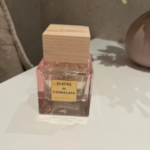 Fleurs de L'Himalaya parfym från Rituals - Säljer en elegant parfymflaska från Rituals med doften Fleurs de L'Himalaya. Flaskan är fyrkantig och genomskinlig med en svagt rosa ton och har en stilren träkork. Perfekt för den som älskar blommiga och fräscha dofter. Passar både till vardags och speciella tillfällen. 🌸