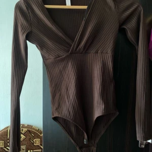 Brun ribbad bodysuit - Säljer en snygg brun ribbad bodysuit med v-ringad design. Den har långa ärmar och är perfekt för höst och vinter. Passar både till vardags och fest!