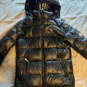 Moncler jacka  - Hej! Säljer denna Moncler jacka (äkta) den har lite skador men inget som syns tydligt den är äkta men köpt begagnad så har inga kvitton,påse mm. Serien har lossnat från landisen men går att sy tillbaka (man får med den) den passar tjejer & killar. 