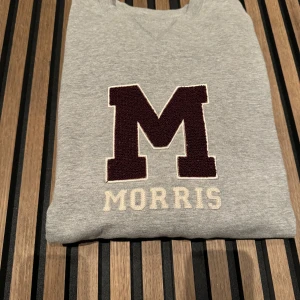 Grå sweatshirt från Morris - Säljer en snygg grå sweatshirt från Morris i storlek Large. Tröjan har ett stort M i vinrött på bröstet och texten 'Morris' under. 