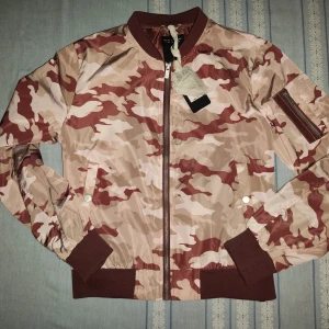 Camouflage bomberjacka - Säljer en snygg bomberjacka från Black Label i ett coolt camouflage-mönster. Jackan har en dragkedja framtill och en ficka med dragkedja på ärmen. Perfekt för höst och vår, och den är i nyskick. Passar perfekt för en casual look!