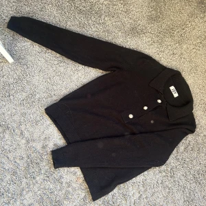 Svart stickad tröja från JDY - Säljer en snygg svart stickad tröja från JDY i storlek XS. Tröjan har långa ärmar och knappar framtill som ger en stilren look. Perfekt för både vardag och lite finare tillfällen. Supermjuk och bekväm att ha på sig!