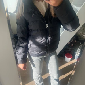 Svart pufferjacka från GANT - Säljer en snygg svart pufferjacka från GANT. Den är perfekt för kyliga dagar och har en dragkedja framtill. Jackan är i storlek 158/164 cm, vilket motsvarar dam S/Xs. Den är i bra skick och använd 1 gång. Nypris är 2100 kr men säljer för 1000 kr.