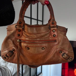 Balenciaga Väska - Snygg brun handväska i skinn med dragkedja och detaljer i metall. Väskan har både handtag och en avtagbar axelrem för flexibilitet. Dustbag medföljer. Dragkedjan är sönder så kom gärna med egna prisförslag! 