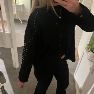 Svart jacka med nitar från ZARA - Snygg svart vårjacka från ZARA med coola nitar längs ärmarna och axlarna. Jackan har långa ärmar och knappar framtill. Använd fåtal gånger. Säljs inte längre på Zara. 