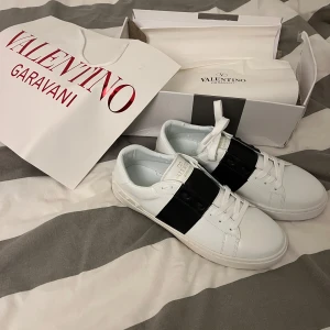 Valentino Garavani sneakers - Snygga vita Valentino Garavani sneakers med en bred svart rem över snörningen. Perfekta för en stilren look.