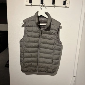 Grå dunväst Uniqlo - Säljer en stilren grå dunväst från Uniqlo i storlek XS. 