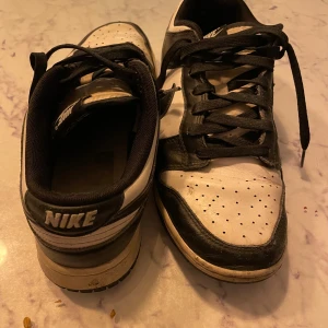 Nike sneakers i svart och vitt - Snygga Nike sneakers i svart och vitt med klassisk snörning. Perfekta för en avslappnad stil. Skorna har en låg profil och är dekorerade med det ikoniska Nike-logotypen på sidan. 