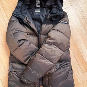 Brun dunjacka från Scotch & Soda - Säljer en brun/svart dunjacka från Scotch & Soda med huva och dragkedja. Jackan är vadderad med PrimaLoft för extra värme vilket gör den väldigt varm. Orginal pris är 1999kr men jag säljer för 800kr, används inte då den inte är min stol, tveka inte på att kontakta vid intresse 😁
