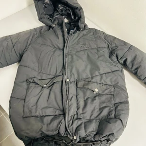 Svart dunjacka från Svea - Säljer en svart dunjacka från Svea i bra skick. Jackan har en mysig huva och praktiska fickor med knappar. Perfekt för kalla vinterdagar. Den har en dragkedja framtill och är quiltad för extra värme. Passar både till vardags och utomhusaktiviteter.