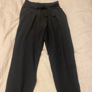 Svarta byxor med knytband - Säljer ett par svarta byxor med snyggt knytband i midjan. Perfekta för både vardag och fest! Materialet känns mjukt och bekvämt.