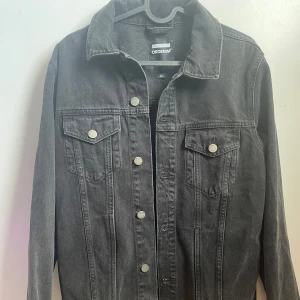 Svart jeansjacka från Dr. Denim - Säljer en snygg svart jeansjacka från Dr. Denim i storlek S. Jackan har en klassisk design med knappar framtill och två bröstfickor med lock. Perfekt för både vår och höst, och funkar till nästan alla outfits. Skicka ett meddelande vid intresse!