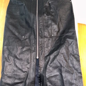 Svart skinnkjol med dragkedja - Säljer en snygg svart skinnkjol oanvänd. Kjolen har en framträdande dragkedja och praktiska fickor framtill. Perfekt för höst och vinter, och kan stylas både upp och ner beroende på tillfälle. Passar bra till både vardag och fest!