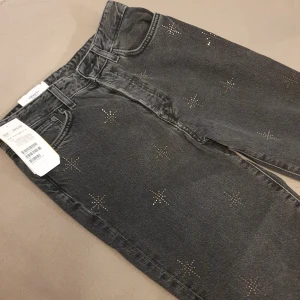 Svarta jeans med silverstenar - Säljer ett par snygga gråsvarta jeans från H&M i vintage fit. Tags kvar så de är aldrig använda! Nypris var 499kr. De har ett coolt stjärnmönster i stenar och knappargylf. Perfekta för en trendig look! 🖤