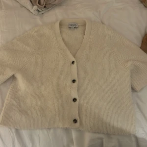 Vit kofta från & Other Stories - Mysig beige kofta från & Other Stories med knappar framtill. Den har en v-ringad design och är tillverkad i ett mjukt material som ger en skön känsla. Perfekt för kyligare dagar.