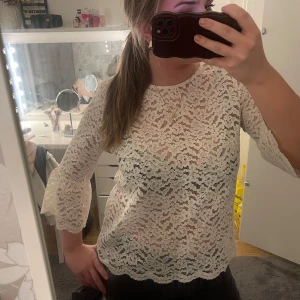 Vit spetsblus - Säljer en elegant vit spetsblus med trekvartsärmar. Blusen har ett vackert blommigt mönster och en feminin passform. Perfekt för en stilren look.