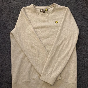 Grå sweatshirt från Lyle & Scott - Säljer en stilren grå sweatshirt från Lyle & Scott i storlek 15/16 år. Tröjan har en klassisk design med rund hals och det ikoniska gula logotypmärket på bröstet. Perfekt för både vardag och skola. Skön och enkel att matcha med det mesta! 🐥