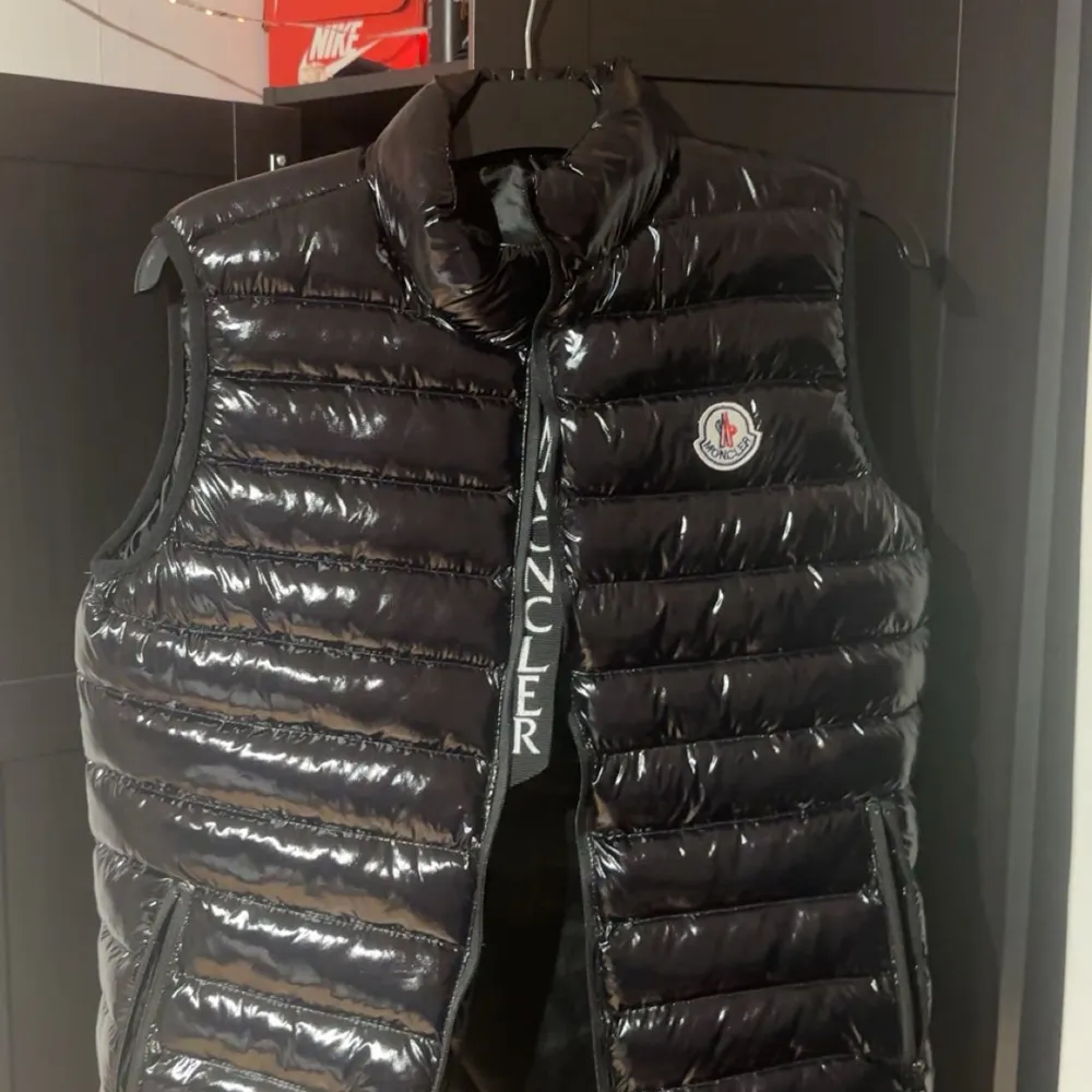 Säljer en snygg och glansig svart dunväst från Moncler. Västen har en dragkedja framtill och ett stilrent märke på bröstet. Perfekt för kyliga dagar när du vill hålla stilen. Passar både till vardags och lite finare tillfällen. 🖤. Jackor.