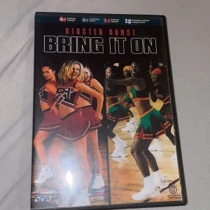 Bring It On DVD - Säljer en DVD av filmen 'Bring It On' med Kirsten Dunst. Filmen handlar om en populär hejarklack och deras kamp mot rivaler. Omslaget visar cheerleaders i röda och gröna dräkter. Perfekt för dig som gillar sportkomedier och 2000-talsfilmer. DVD:n har specialfunktioner och är rekommenderad från 11 år.