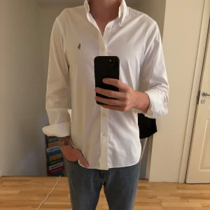 Vit skjorta från Ralph Lauren - Snygg vit skjorta från Ralph Lauren med klassisk krage och broderad logotyp på bröstet. Skjortan har långa ärmar och knappar framtill. Perfekt för en stilren look. Den är i size small men fits medium också beroende på fit, den är toppskick.