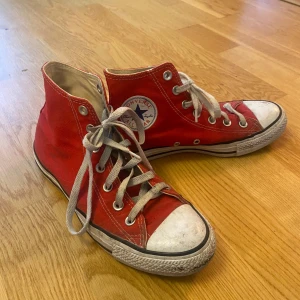 Röda Converse All Star sneakers - Säljer ett par klassiska röda Converse All Star sneakers i bra skick. De har en hög modell med snörning och den ikoniska loggan på sidan. Perfekta för både vardag och fest! Lite slitna på tårna men annars i fint skick. Storlek 40