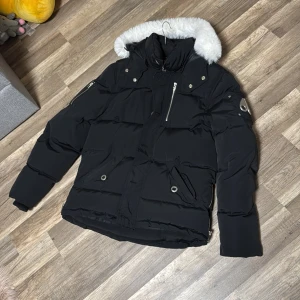 Svart dunjacka från Moose Knuckles - Säljer en svart dunjacka från Moose Knuckles i mycket bra skick. Jackan har en snygg pälskantad huva och flera praktiska fickor med dragkedja och knappar. Perfekt för kalla vinterdagar! 🖤har knappt använt jackan den är i ny skicka och jackan är äkta 