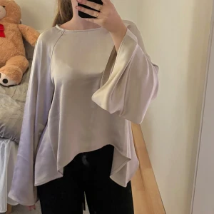Topp - Säljer en superfin champagne  blus i satinmaterial. Den har vida ärmar som ger en elegant touch och en lös passform som är perfekt för både vardag och fest.  Mycket fint material. 