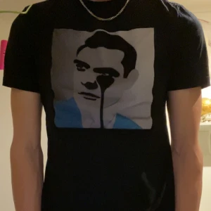 Limitato - Snygg svart t-shirt från Limitato med ett unikt tryck av ett ansikte i grått och blått på framsidan. Tillverkad av 100% merceriserad bomull för en mjuk och lyxig känsla. Perfekt för dig som vill ha något stilrent men med en twist.