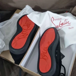 Svarta sneakers med nitar från Christian Louboutin - Snygga svarta sneakers från Christian Louboutin med ikoniska röda sulor och nitar på tån. Skorna har snörning och är tillverkade i skinn, vilket ger en lyxig känsla.