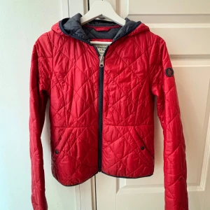 Röd quiltad jacka från Abercrombie & Fitch - Snygg röd quiltad jacka från Abercrombie & Fitch med huva och dragkedja. Perfekt för kyliga dagar med vattenavvisande material och isolering. Jackan har långa ärmar och praktiska fickor med knappar. Köpt i USA 