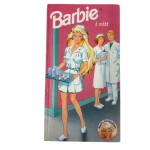 Barbie i vitt - En charmig bok med Barbie som sjuksköterska, klädd i en vit uniform. Omslaget är rosa med en illustration av Barbie och två andra sjuksköterskor. Perfekt för Barbie-fans och samlare!
