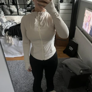 Beige långärmad tröja med dragkedja - Säljer en snygg beige långärmad tröja med dragkedja framtill. Den är tight och perfekt för både vardag och träning. Tröjan har en hög krage och är i mycket bra skick. Perfekt för höst och vår!
