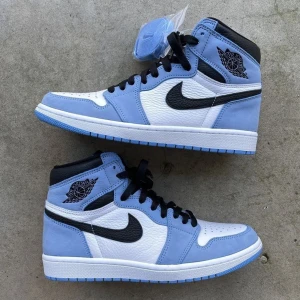Nike Air Jordans UNC OG HIGH - Säljer ett par snygga Nike Air Jordans i blått och vitt. Skorna har en klassisk design med svart swoosh och svarta snören. Perfekta för både vardag och fest! De är i nytt skick och kommer med extra skosnören. Storlek är ej specificerad, men de ser ut att vara i herrstorlek. Har tyvärr inte box kvar och har använt dom 3 gånger men de är helt oskadade och fräscha . !säljer lågt pris för vill bli av med dom!