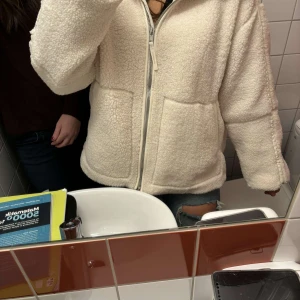 Beige teddyjacka med dragkedja - Slutsåld populär Mysig beige teddyjacka med dragkedja framtill och hög krage. Perfekt för kyliga dagar med sin fluffiga och varma design. Jackan har två stora fickor och en avslappnad passform. Säljer pågrund av att den ej passar. Kan diskutera pris och skriv för egna bilder
