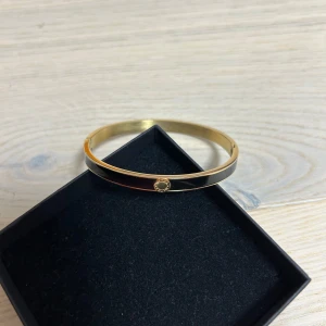 Elegant guldarmband med detalj - Säljer ett stilrent och elegant guldarmband med en fin detalj framtill. Armbandet är i mycket bra skick och passar perfekt för både vardag och fest. Det är enkelt att matcha med andra smycken och ger en lyxig touch. BY Jolima