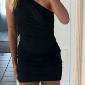 Svart oneshoulder klänning - Snygg svart oneshoulder klänning som är perfekt för en utekväll. Den har en tight passform och kort längd som framhäver figuren. Klänningen är stilren och enkel, vilket gör den lätt att matcha med olika accessoarer.