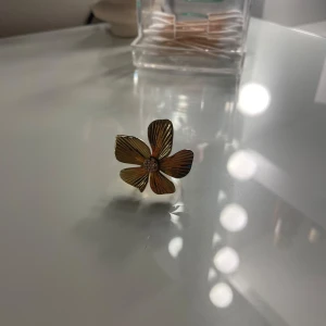 Guldfärgad blomring - Säljer en superfin guldfärgad ring formad som en blomma. Den har detaljerade blad och en glittrig mitt som verkligen fångar ljuset. Kuster var och gjprd av rostfri stål. Ej några defekter förutom att 2 diamanter i mitten saknas men det märks inte