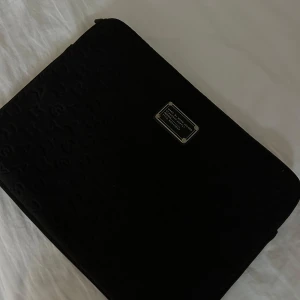 Svart datorväska från Marc by Marc Jacobs - Snygg svart datorväska från Marc by Marc Jacobs med präglad logotypdesign. Perfekt för att skydda din laptop med stil. Väskan har en elegant och minimalistisk look.