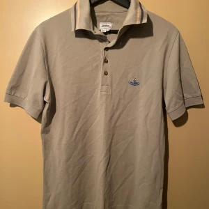 Vivienne Westwood Pikétröja - En Vivienne Westwood pikétröja i en olivgrön färg med en broderad logga på bröstet. Tröjan är i storlek medium och passar true to size utan några  skador eller defekter. Känn dig fri att fråga om du undrar något mer!