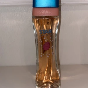 Star Parfym - Säljer en cool parfymflaska med en unik design. Flaskan är genomskinlig med en blå och rosa kork. På framsidan finns en söt bild av sockervadd och små stjärnor. Perfekt för dig som gillar en lekfull och söt stil! Luktar sockervadd😍